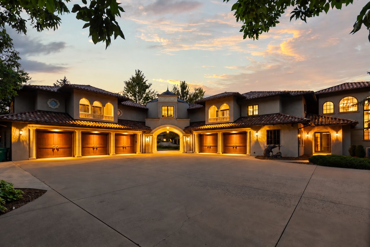 Mediterranean-style residence with an arched entrance and illuminated garage doors at dusk.