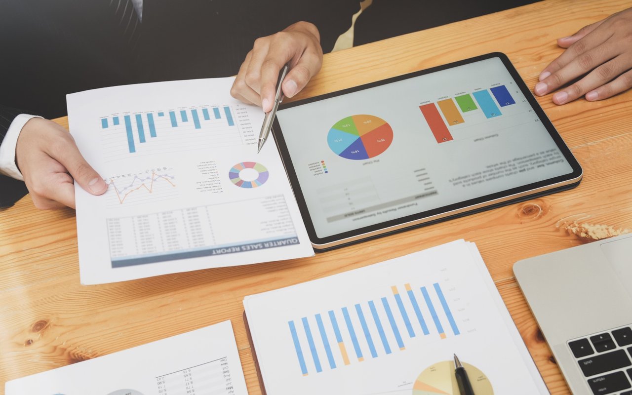 People review sales charts and reports on paper and a tablet.