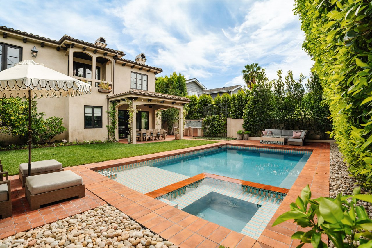 Backyard pool beside a two-story stucco home, with a tiled shallow entry and terracotta patio.