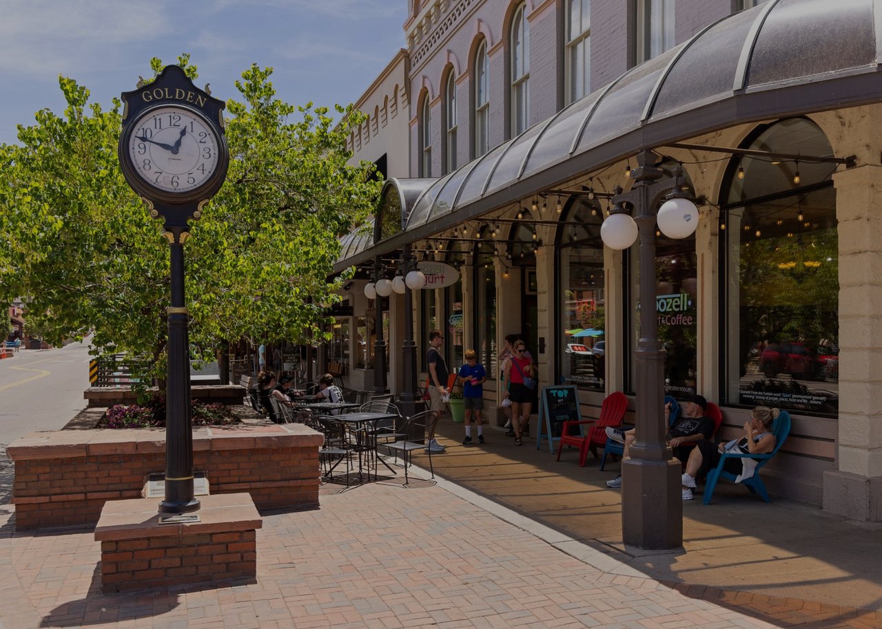 Downtown Golden street clock beside a tree-lined café patio.
