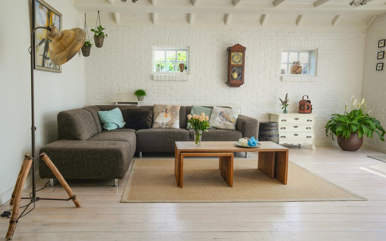 Living room with a gray sectional, wood coffee table, white brick walls, and exposed ceiling beams.