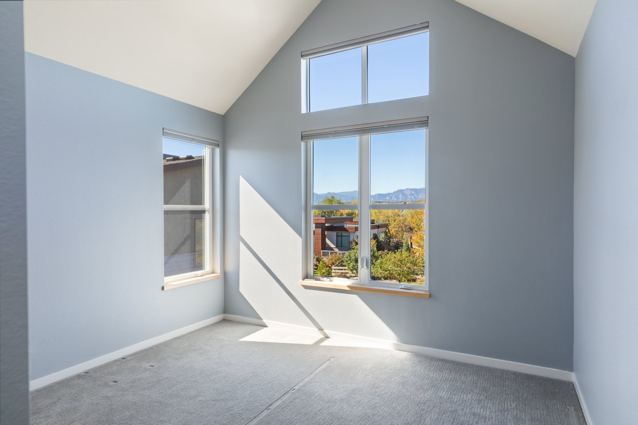 Bedroom with blue-gray walls, a vaulted ceiling, and tall windows
