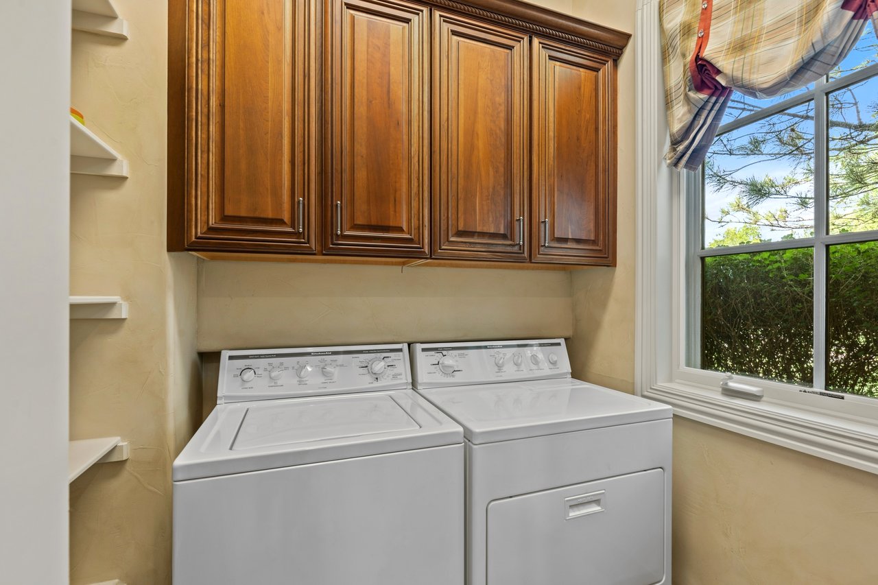 Guest-house laundry room with a washer and dryer, dark wood cabinets, and a large window.