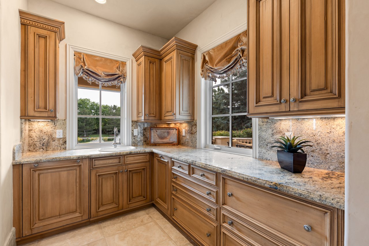 Kitchen with ornate wood cabinetry, granite counters, and a corner sink beneath two windows.