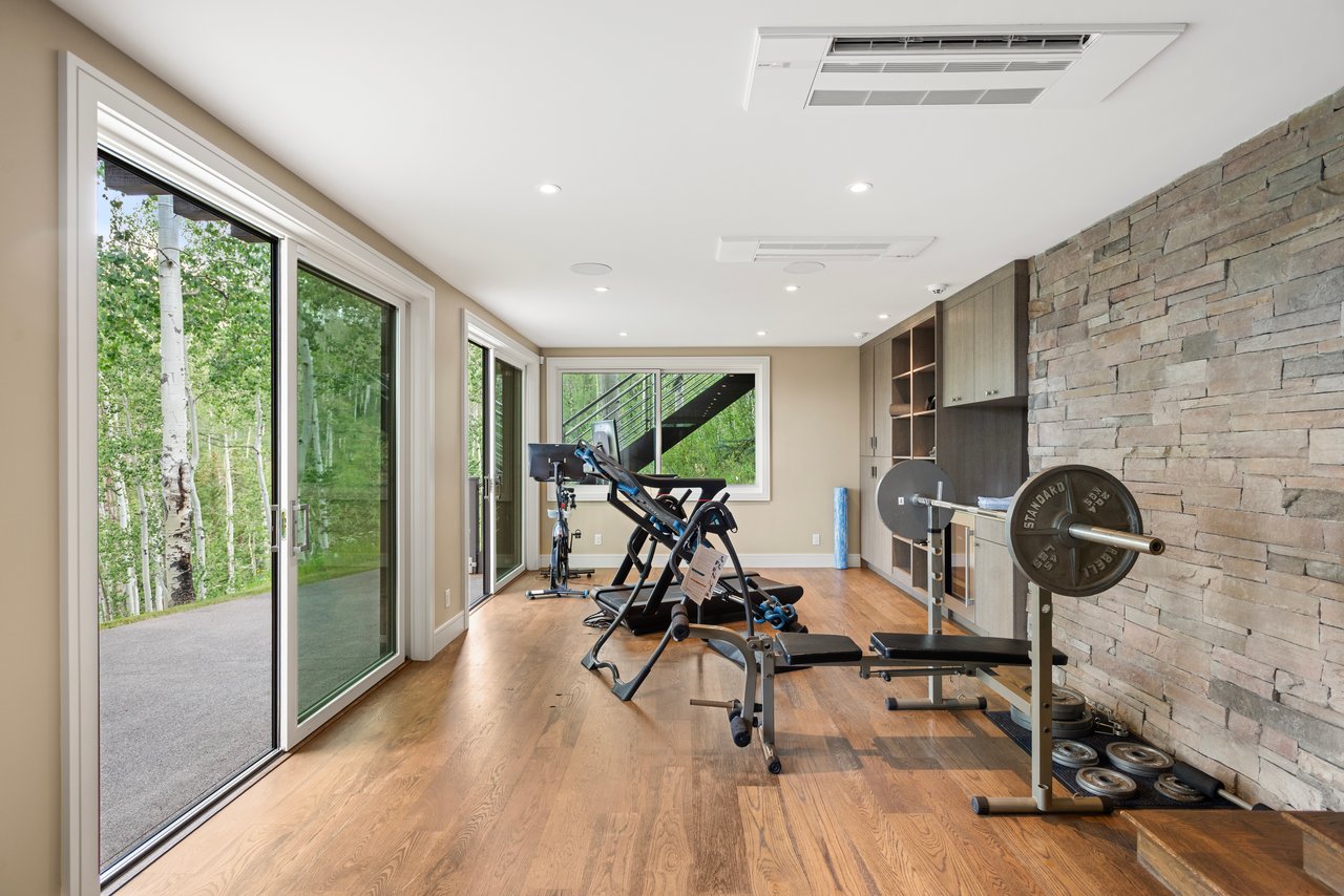 Home gym with a weight bench and barbell beside a stone wall and sliding glass doors.