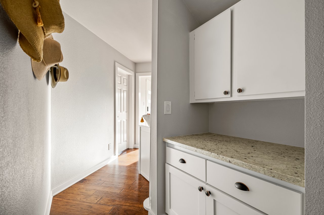 Hallway with white built-in cabinets, a stone countertop, wood flooring, and hats on wall hooks.