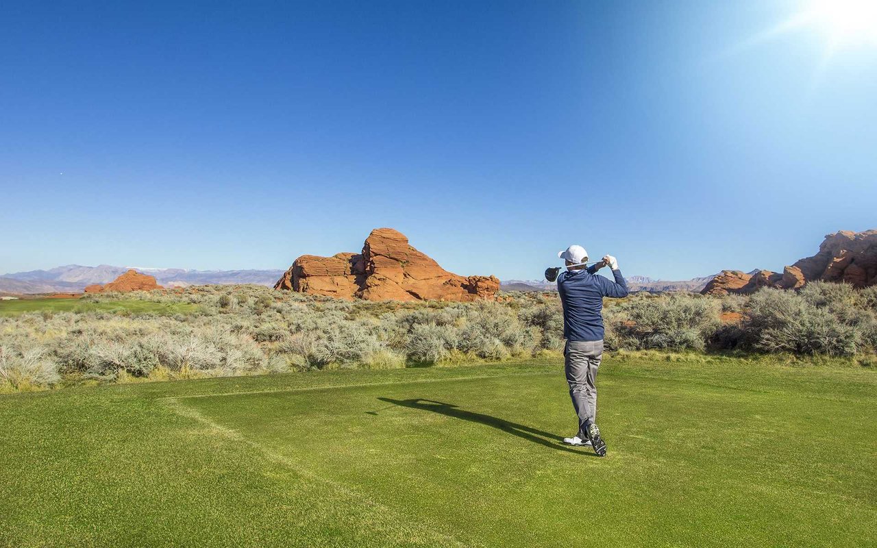 Golfer on a green with red rock formations and desert scrub.