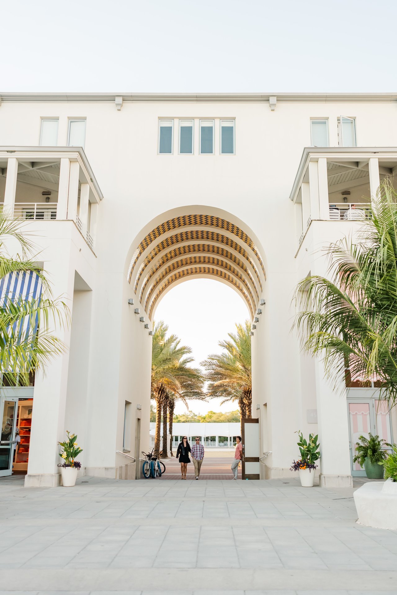 Seaside's iconic white postmodern beach pavilion arch framing a palm-lined walk toward the Gulf of Mexico on 30A, Florida