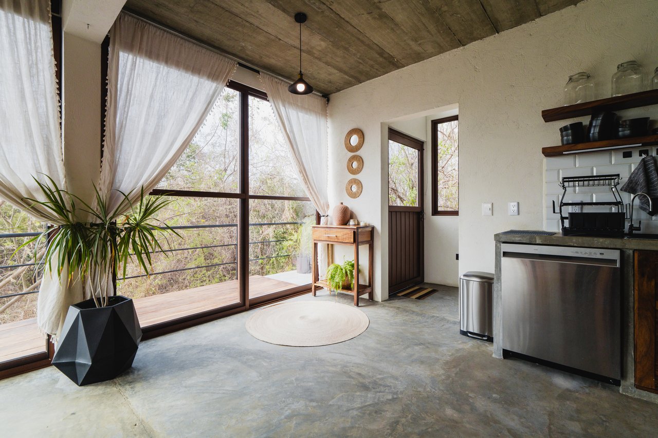 Kitchen with concrete finishes, large curtained windows, and a view onto a wooden deck.