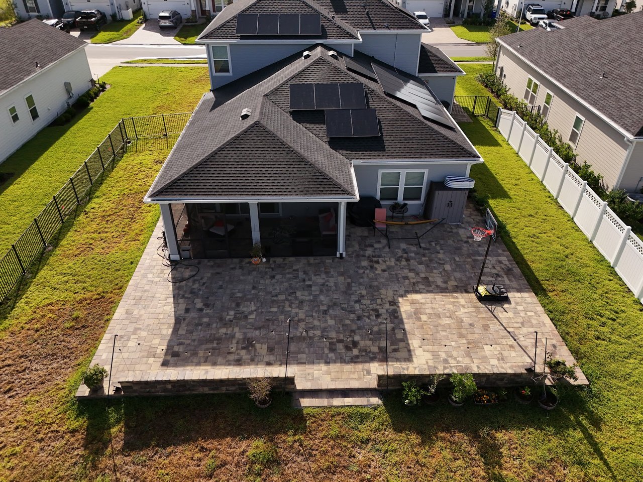 Aerial view of a home’s backyard with a broad paver patio, screened lanai, and solar panels.