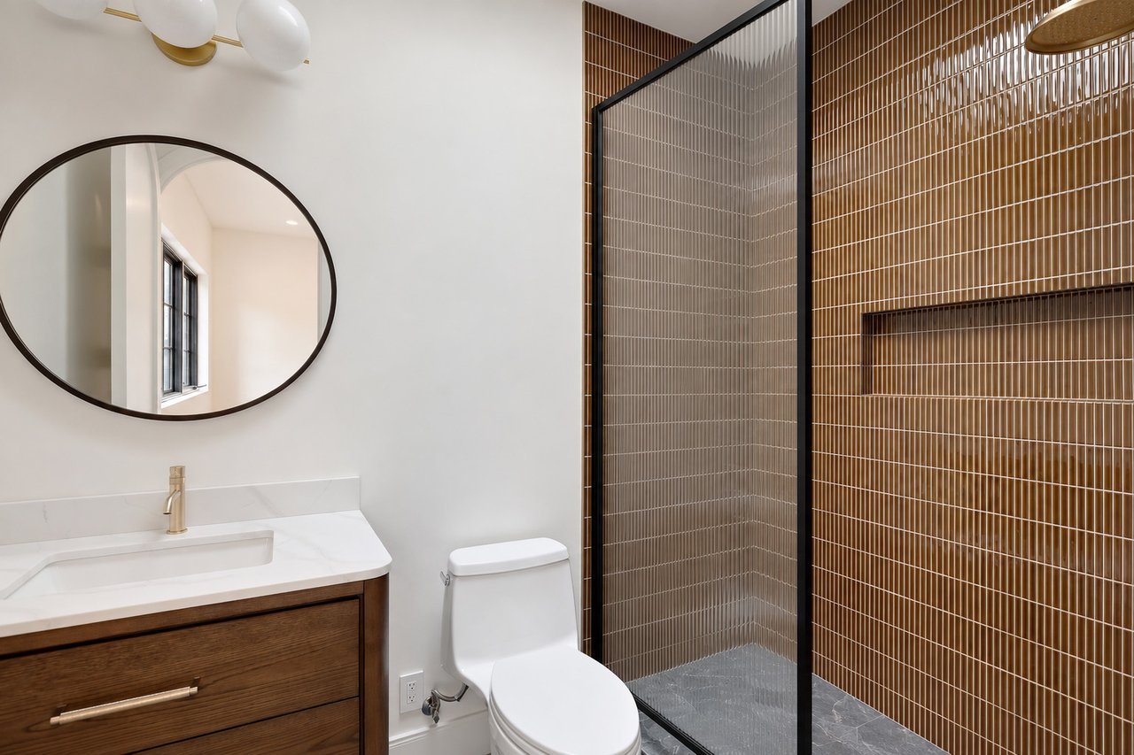 Modern bathroom with a dark wood vanity and brown-tiled walk-in shower.