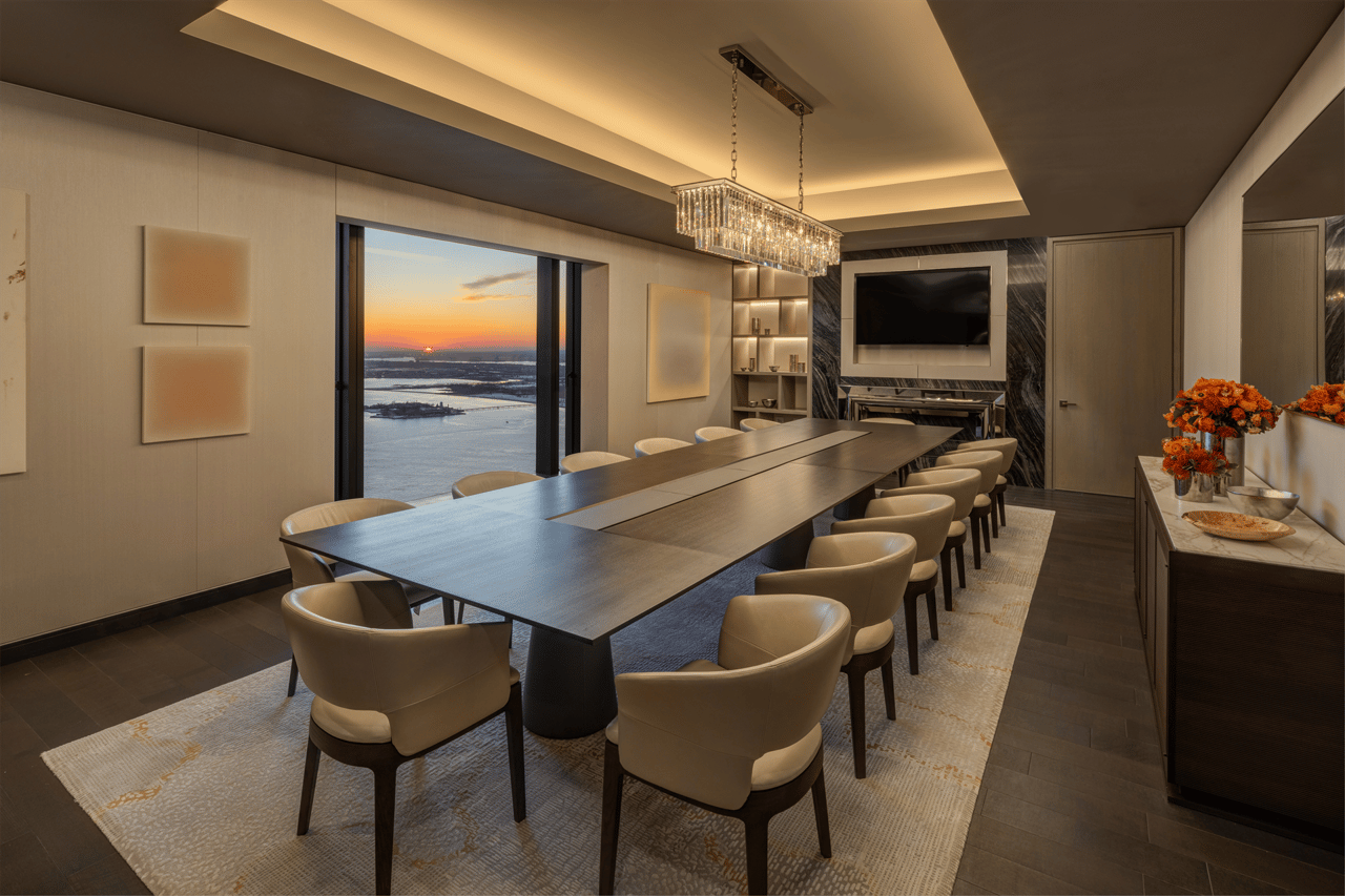 Furnished dining room with a long table and sunset water views through expansive windows.