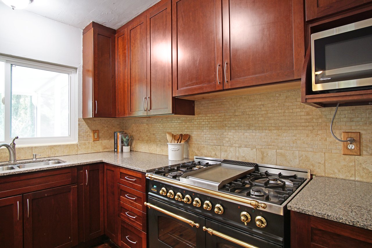 Kitchen with dark wood cabinets, granite countertops, and stainless steel appliances. A large window provides natural light, creating a warm atmosphere.
