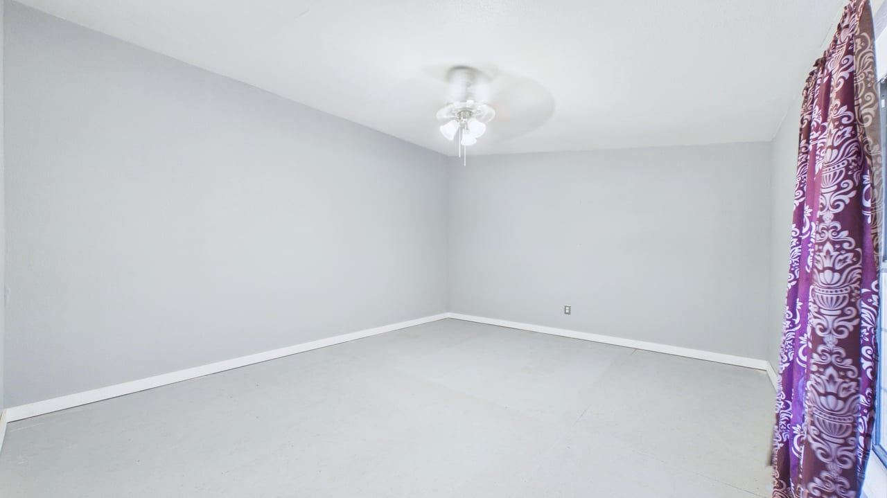 Empty room with gray walls, pale flooring, ceiling fan, and purple patterned curtain.