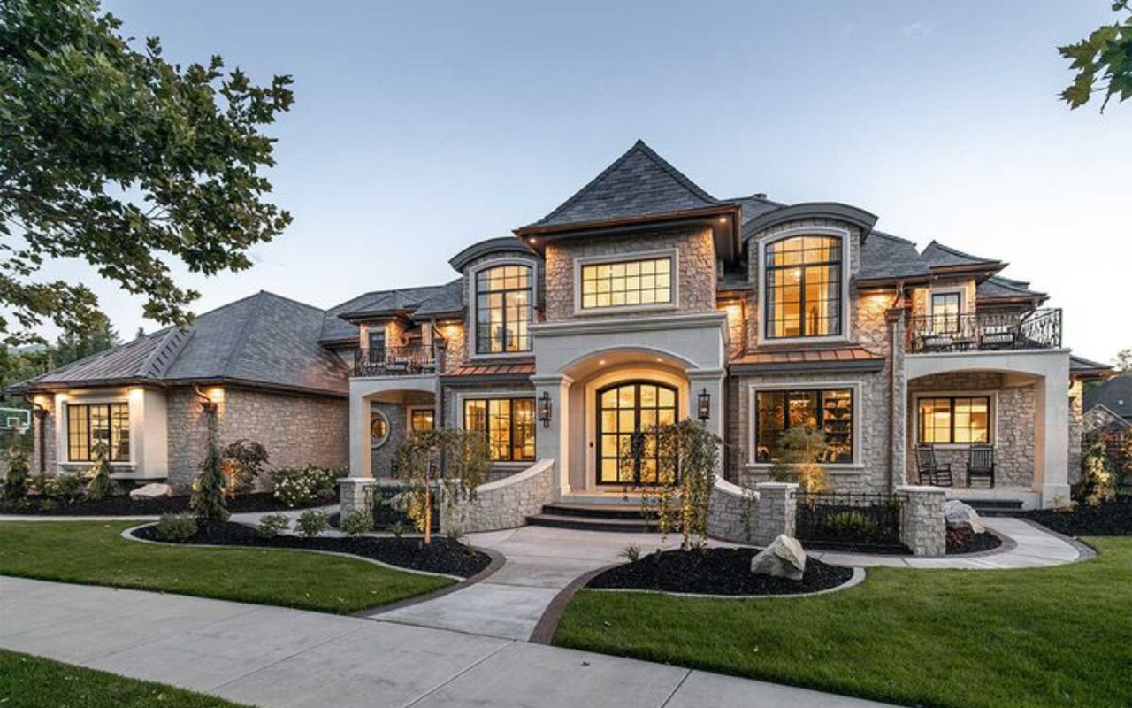 Two-story stone home with an arched entrance, illuminated windows, and landscaped lawn.