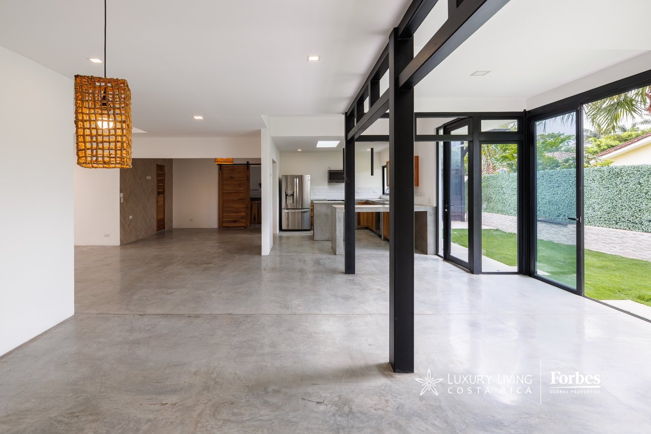 Open-plan home interior with polished concrete floors, black steel framing, and glass doors onto a garden.