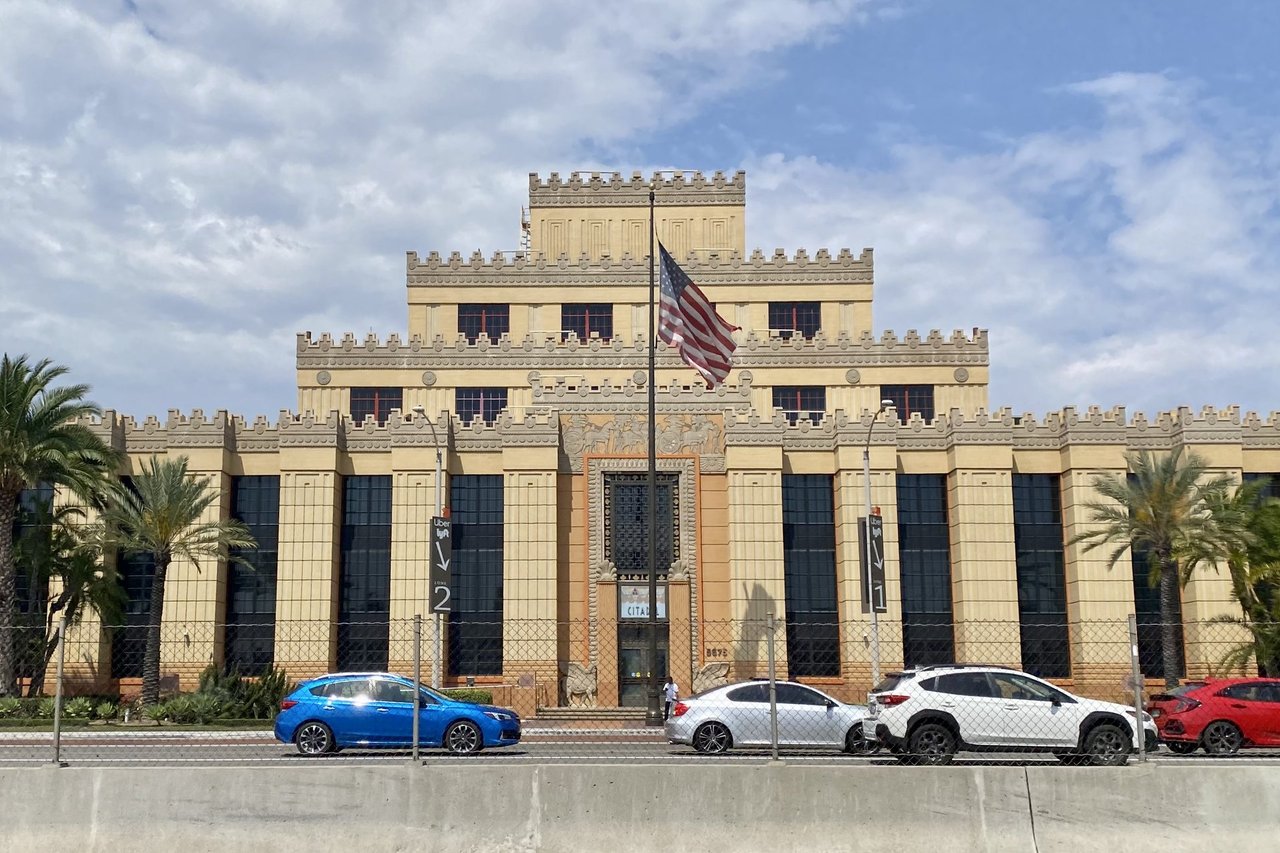 Citadel Outlets frontage in Commerce with flags and passing cars, May 2023