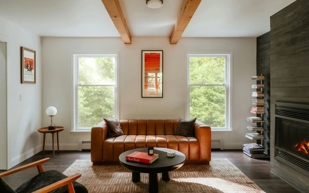 Living room with a caramel leather sofa, exposed wooden beams, and a dark paneled fireplace.