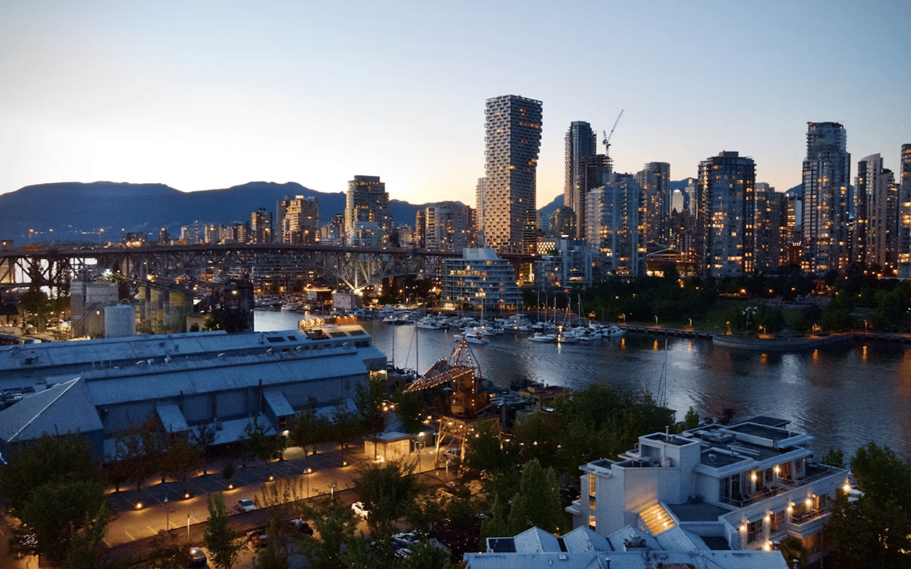 Vancouver waterfront at dusk, with downtown towers, a bridge, and boats in the harbor.