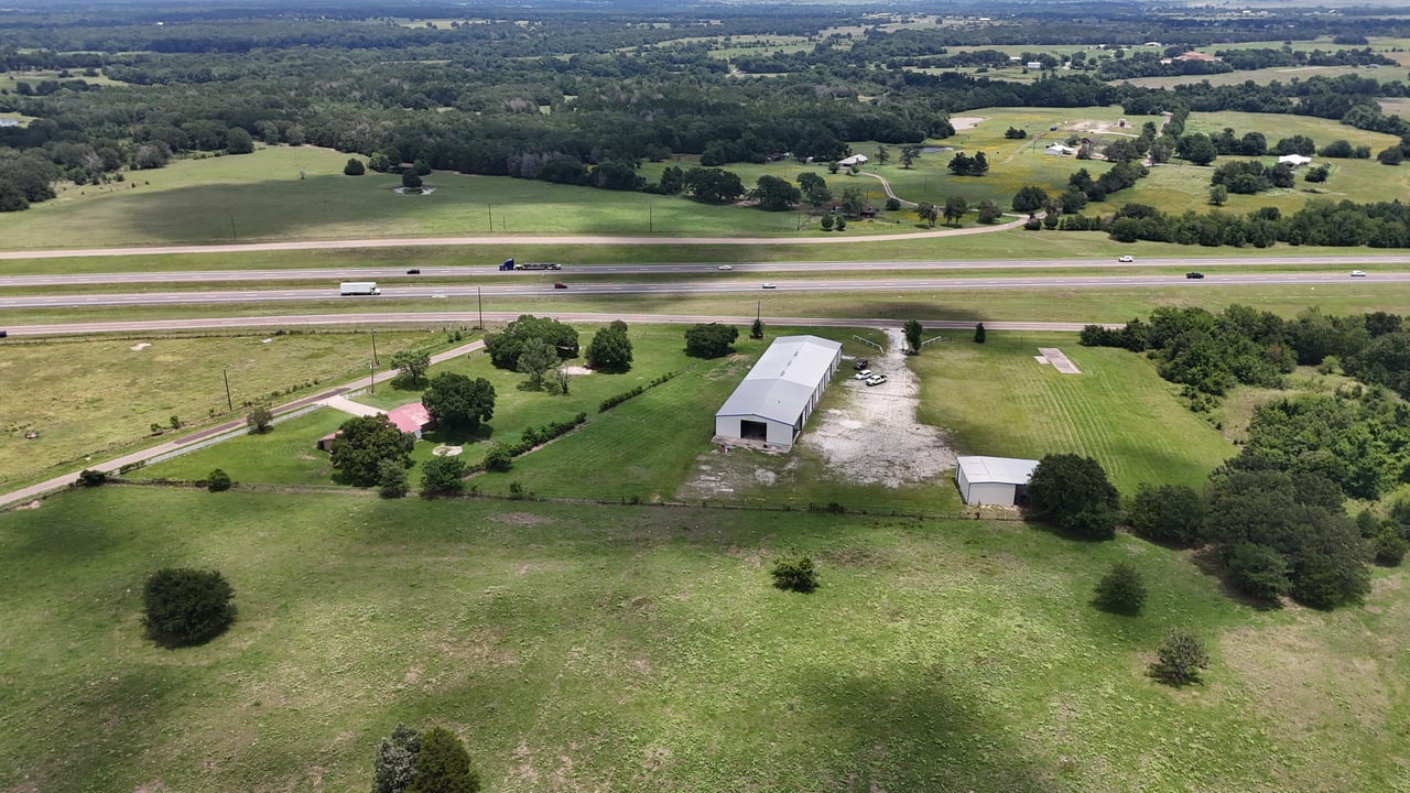Aerial view of a rural commercial property with two metal buildings beside a highway.