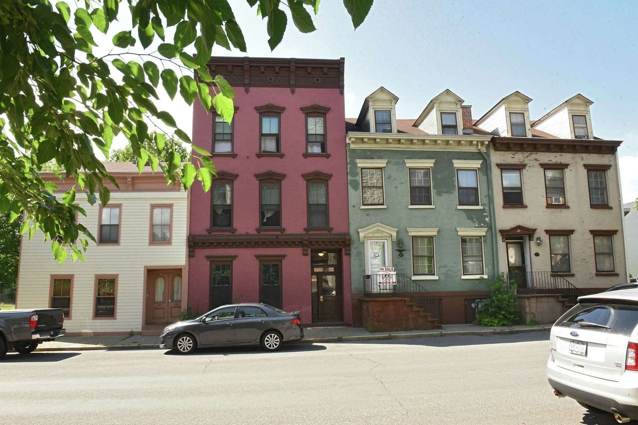 Colorful attached homes with dormer windows and a For Sale sign on the green facade.