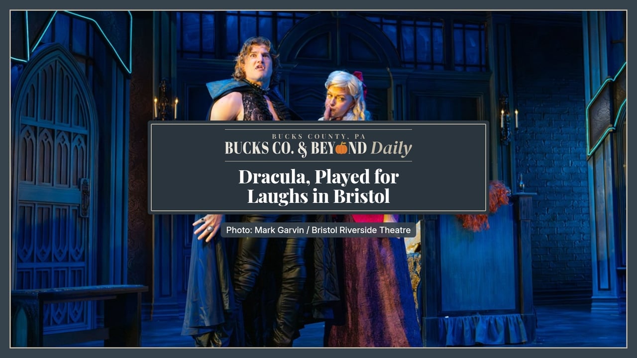 Bucks Co. & Beyond Daily: Dracula, Played for Laughs in Bristol. Stage photo from Bristol Riverside Theatre's Dracula: A Comedy of Terrors, with Count Dracula in a black cape, lace shirt and leather pants looking startled while a blonde castmate in a white lace blouse and pink skirt shushes him, on a blue-lit gothic set.