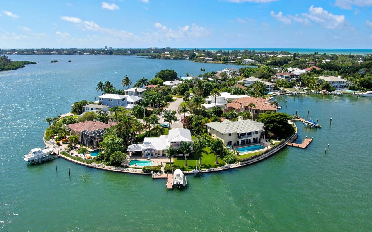 Aerial view of waterfront homes, docks, and pools on a residential island surrounded by blue water.