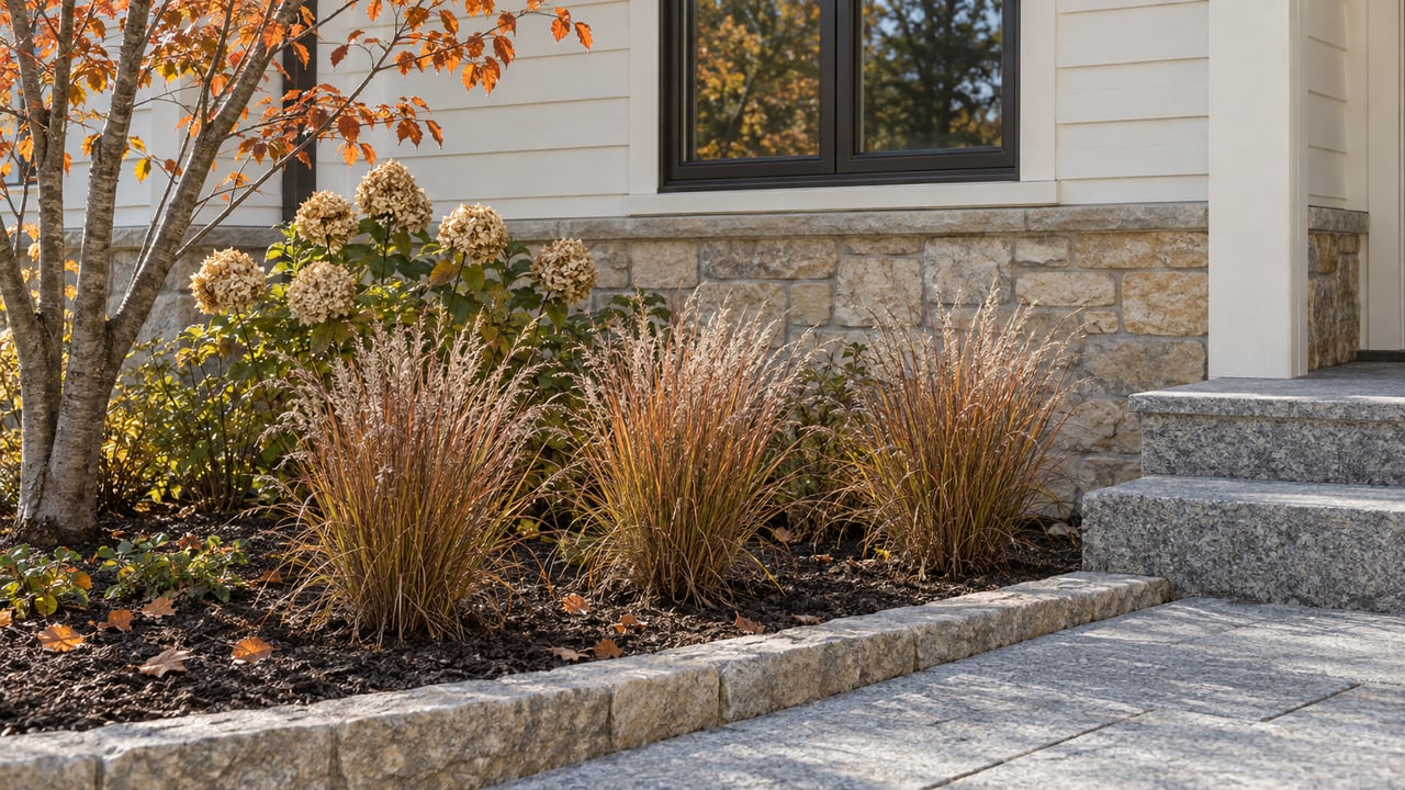 Copper-colored little bluestem and dried hydrangea blooms beside a limestone foundation, ivory siding, and granite entry steps.