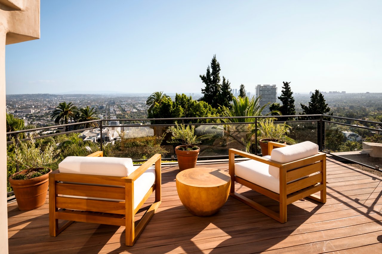 Outdoor terrace with a wood deck, cushioned lounge chairs, and an expansive city view.