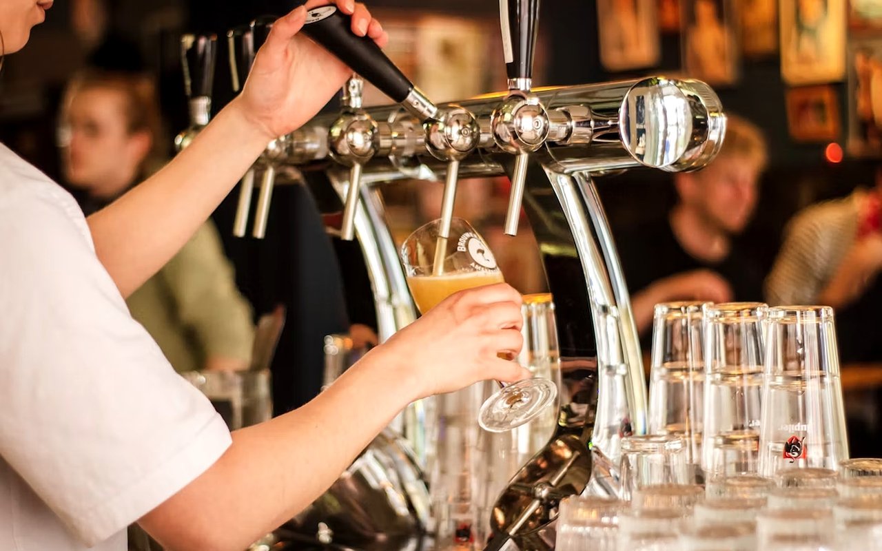 Bartender pours draft beer from chrome taps beside rows of glasses.