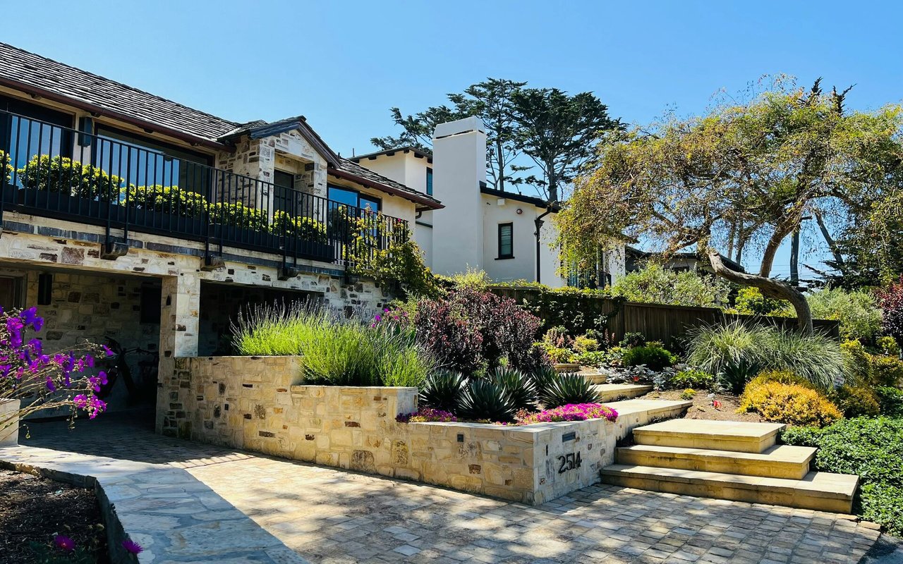 Two-story stone-and-stucco home with a black balcony, landscaped entry, and broad stone steps.
