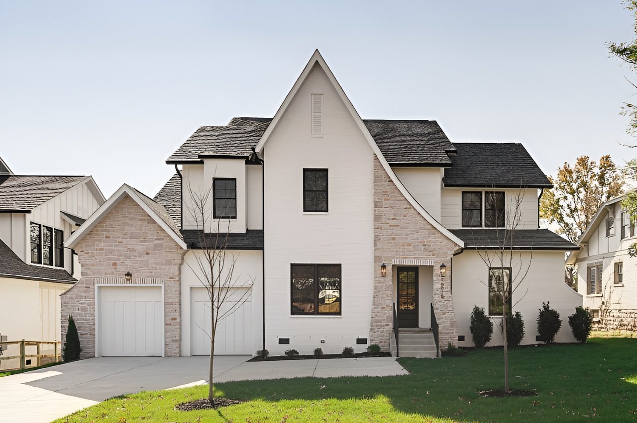 Two-story white house with stone accents, steep gables, attached garage, and front lawn.