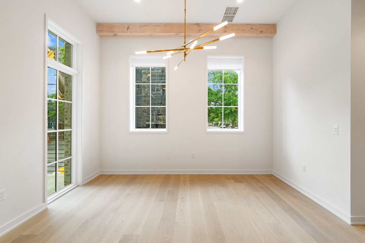 Empty dining room with pale wood floors, tall windows, and a modern branching chandelier.