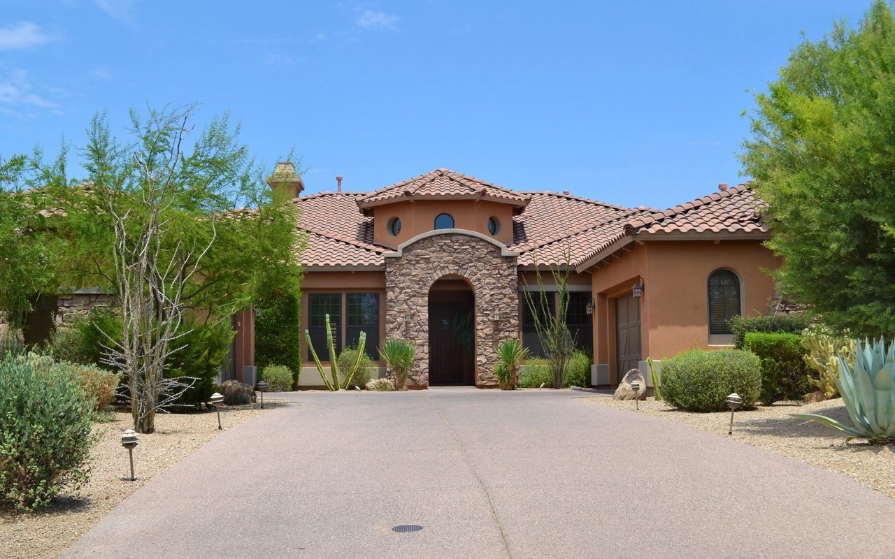 Stucco home with a stone arched entry, red tile roof, and desert landscaping.