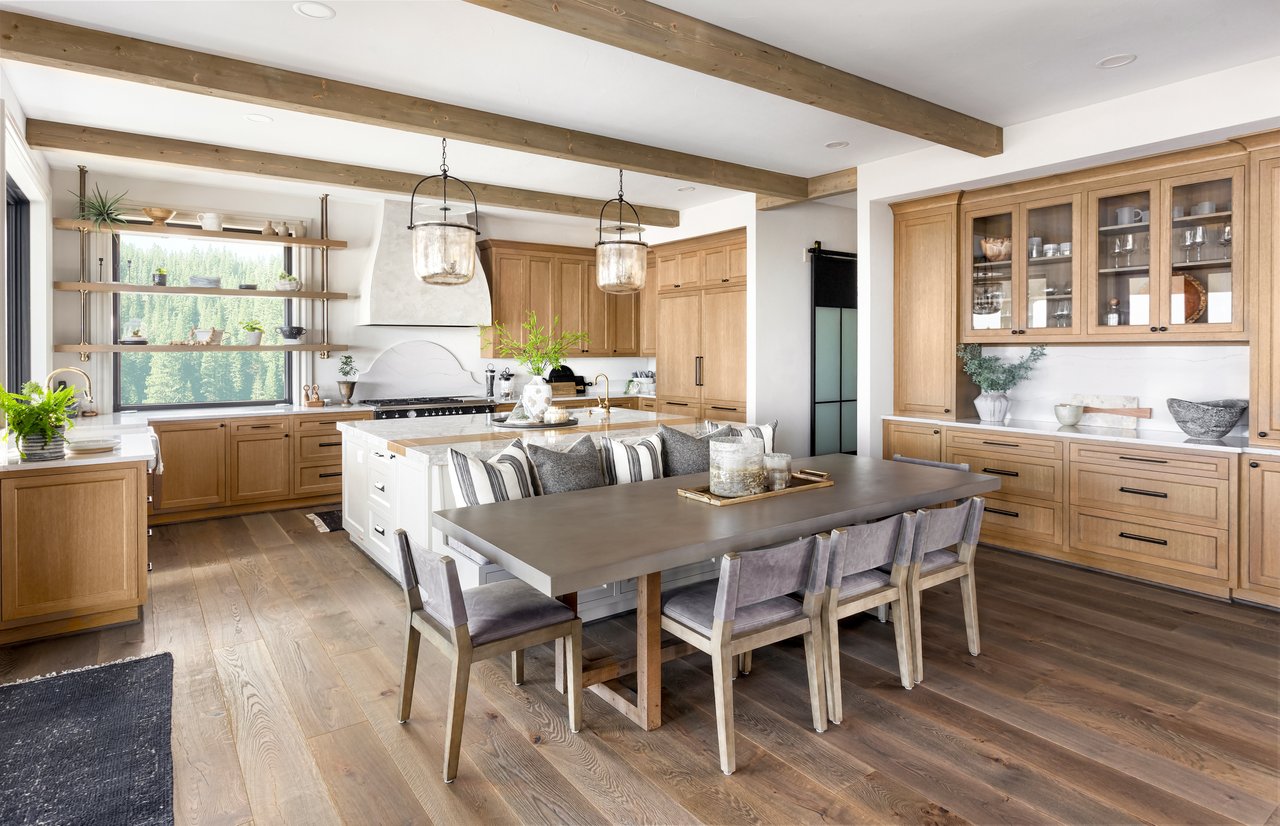 Kitchen and dining area with warm wood cabinetry, a large island, and a wooded view through the window.