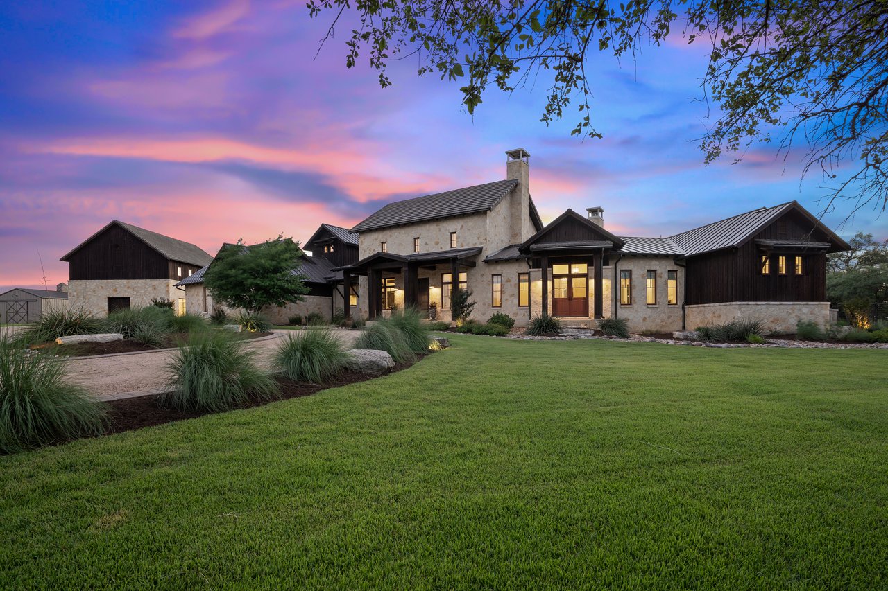Twilight front elevation of this hill country estate at 335 Winning Colors in Key Ranch at the Polo Club, Austin, TX, built by John Siemering Homes, framed by mature oak trees.