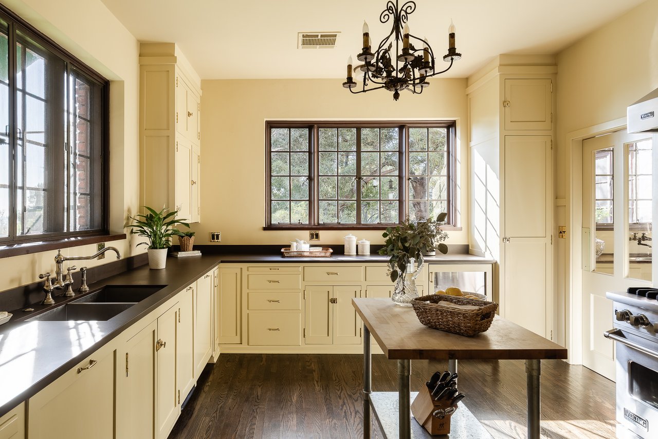 Kitchen with cream cabinets, dark countertops, a farmhouse sink, and a wooden island table.