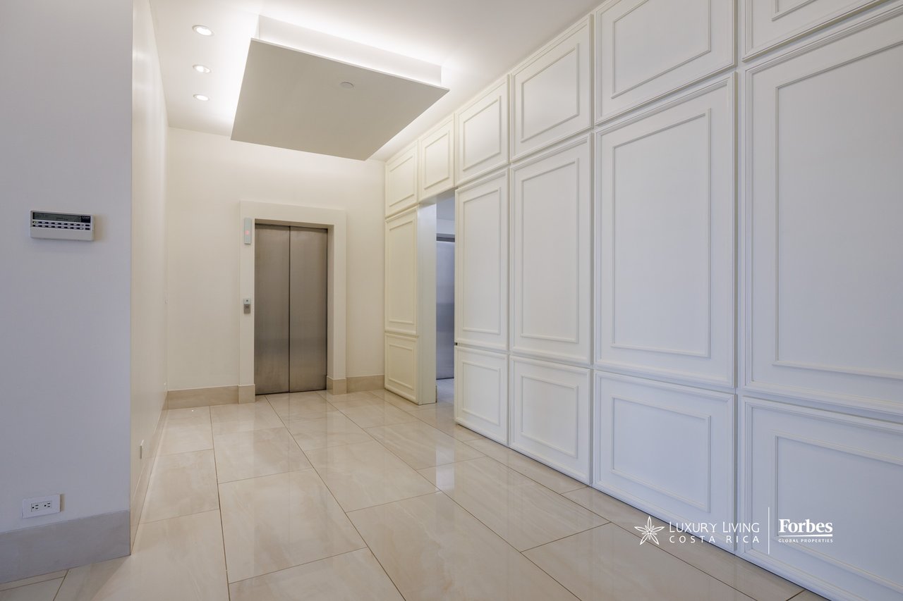 Apartment entry foyer with a stainless-steel elevator and ornate white paneled walls.