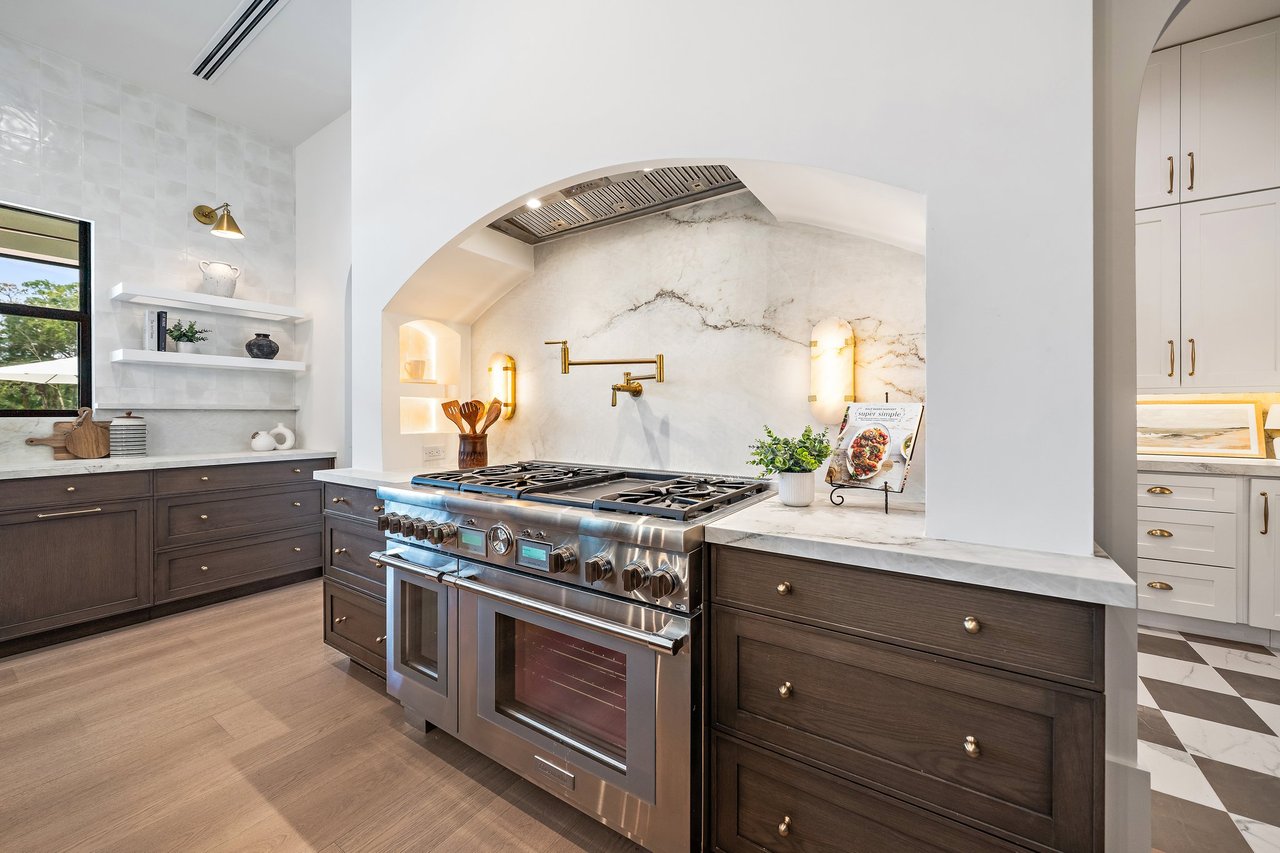Luxury kitchen with a stainless steel range, arched hood, marble backsplash, and dark wood cabinetry.