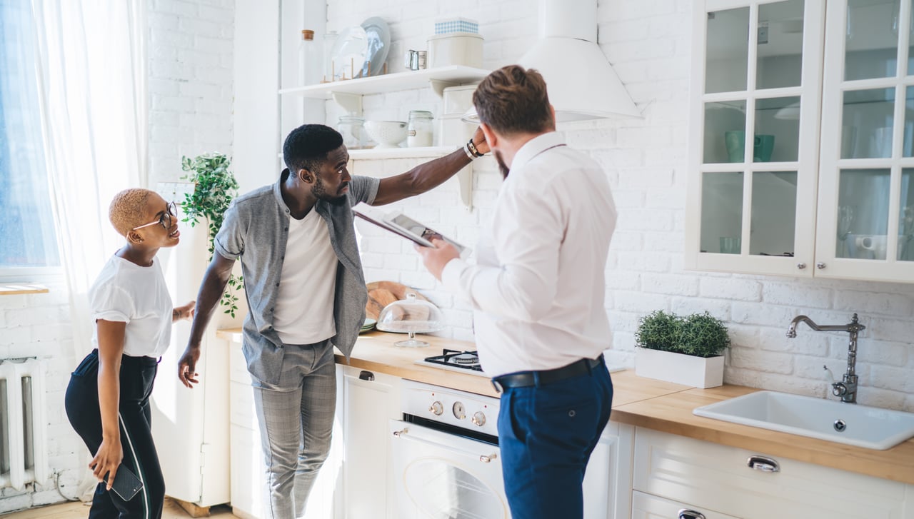 Young couple touring a home with a real estate agent and inspecting the kitchen.