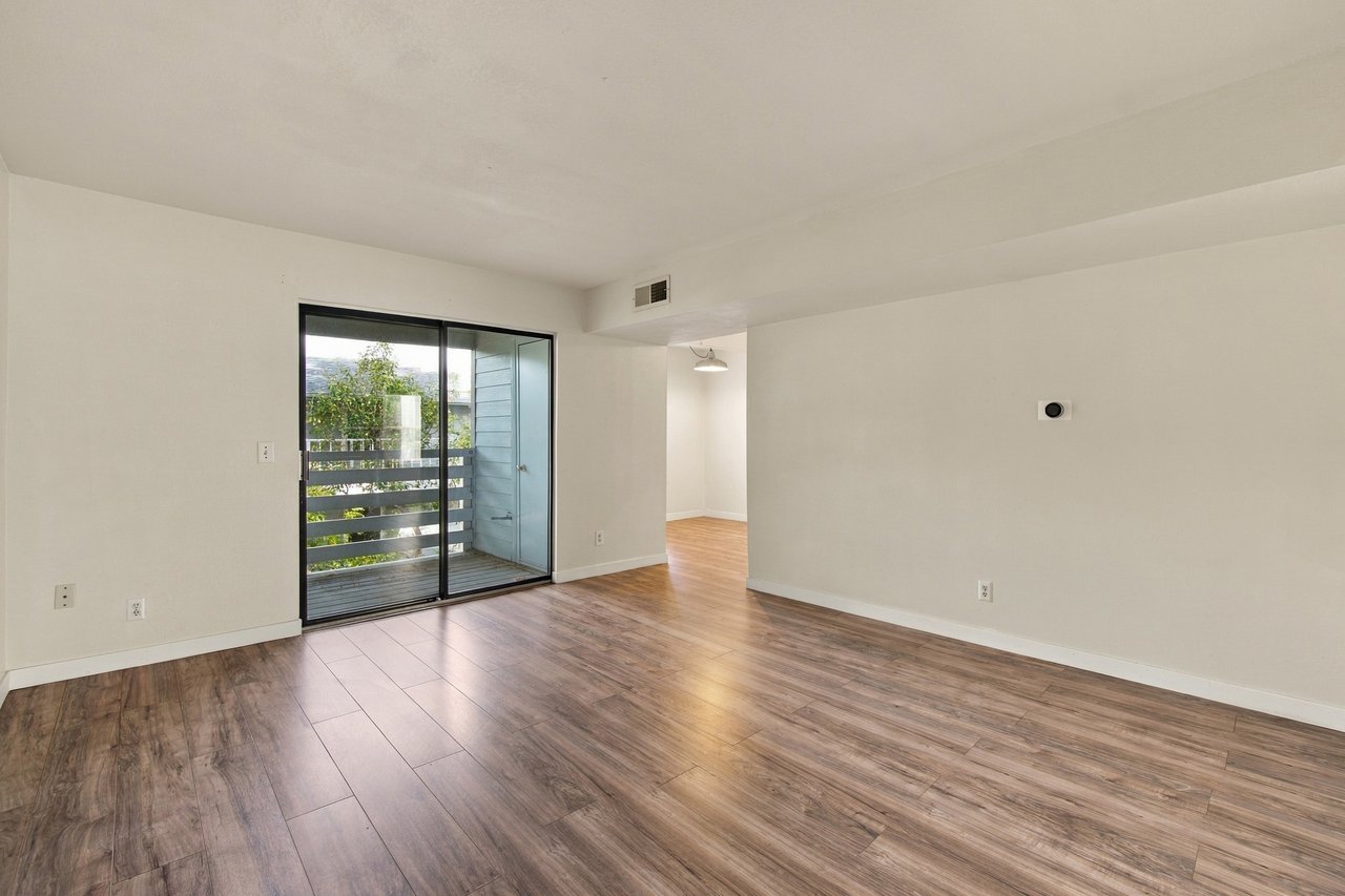Vacant living room with wood-look flooring and a sliding glass door to the balcony.