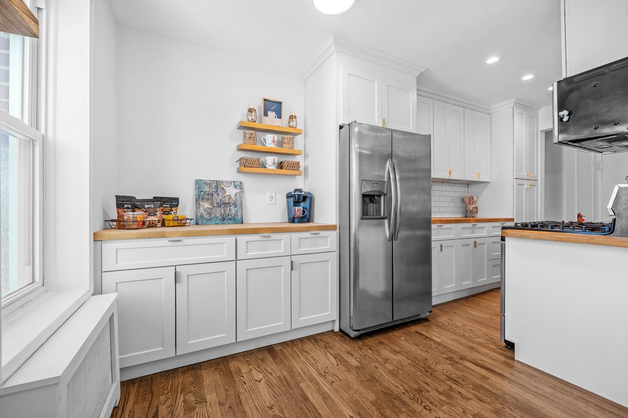 Bright kitchen with white cabinets, butcher-block counters, stainless steel appliances, and hardwood floors.
