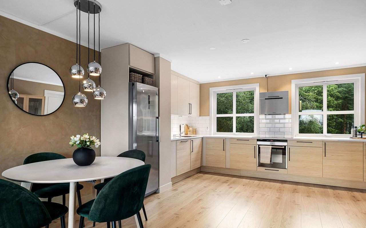 Modern kitchen with light wood cabinets, stainless steel appliances, large windows, and a round dining table.