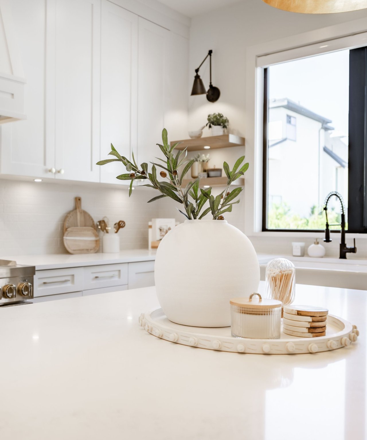 Bright white kitchen with a large island and a vase of olive branches on a tray.