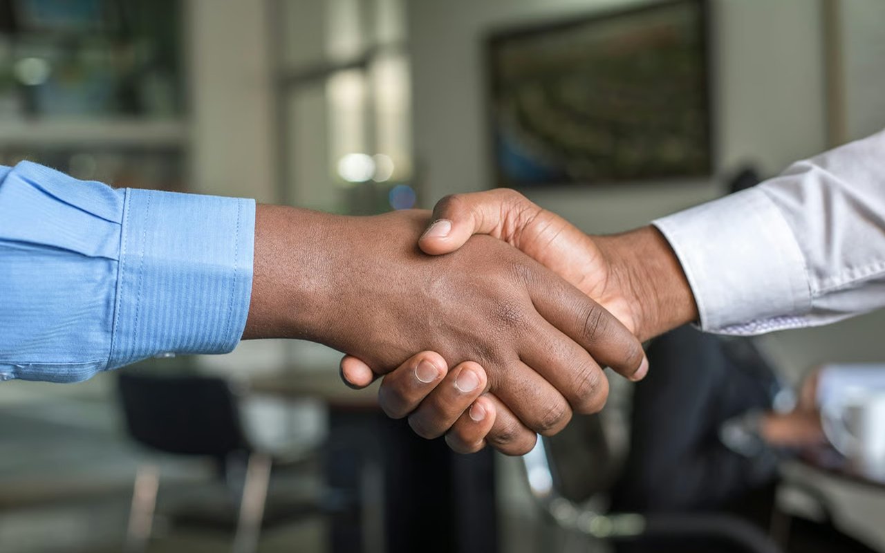 Two people shake hands, one wearing a blue sleeve and the other a white sleeve.