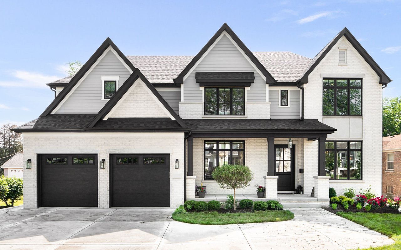 Two-story white brick and gray house with steep gables, black trim, and a two-car garage.