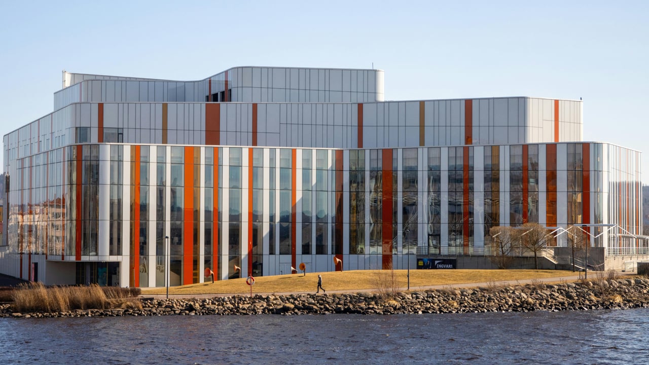Modern glass commercial building with orange facade accents beside the water.
