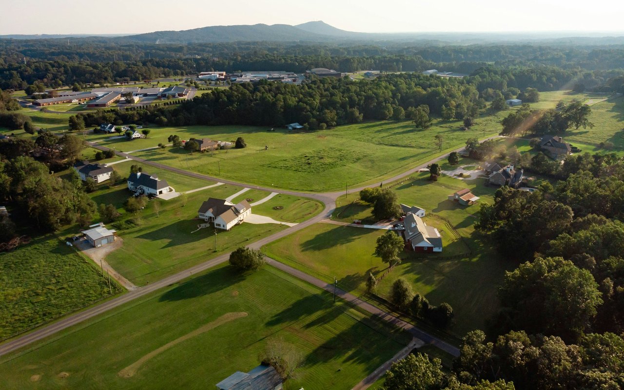 Aerial view of a rural neighborhood with scattered homes, green fields, and wooded hills.
