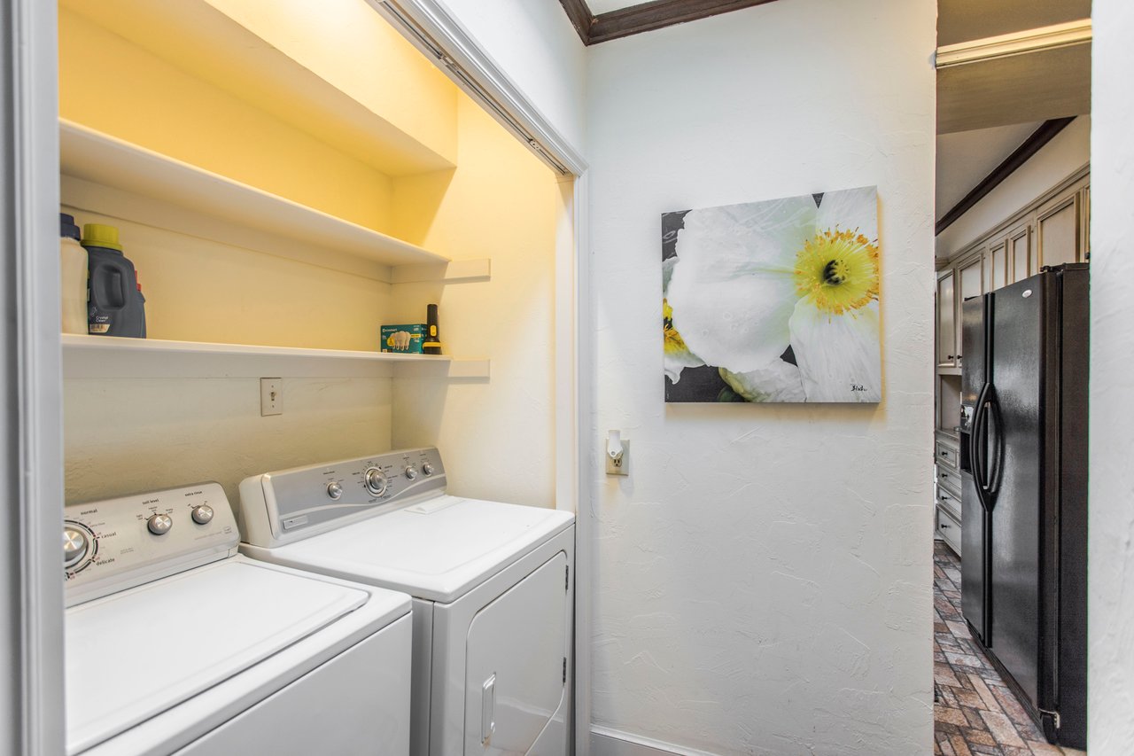 Laundry area with a white washer and dryer, open shelves, and a view into the adjoining kitchen.