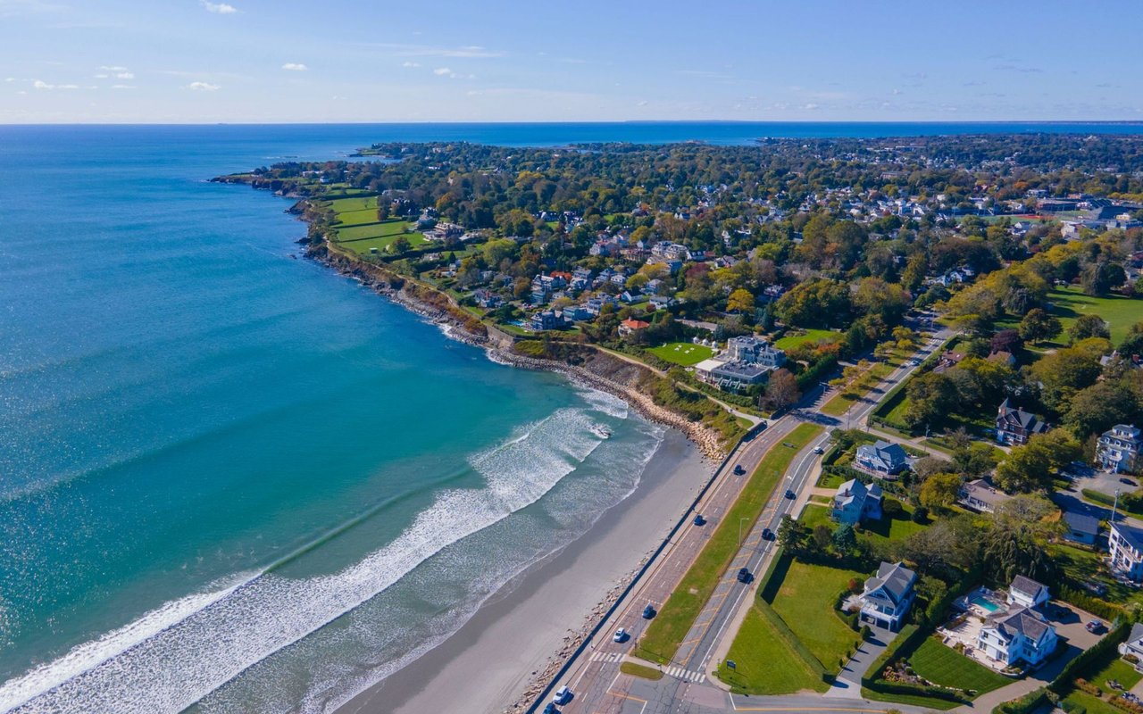 Aerial view of a coastal neighborhood with a sandy beach, ocean waves, and homes along the shore.